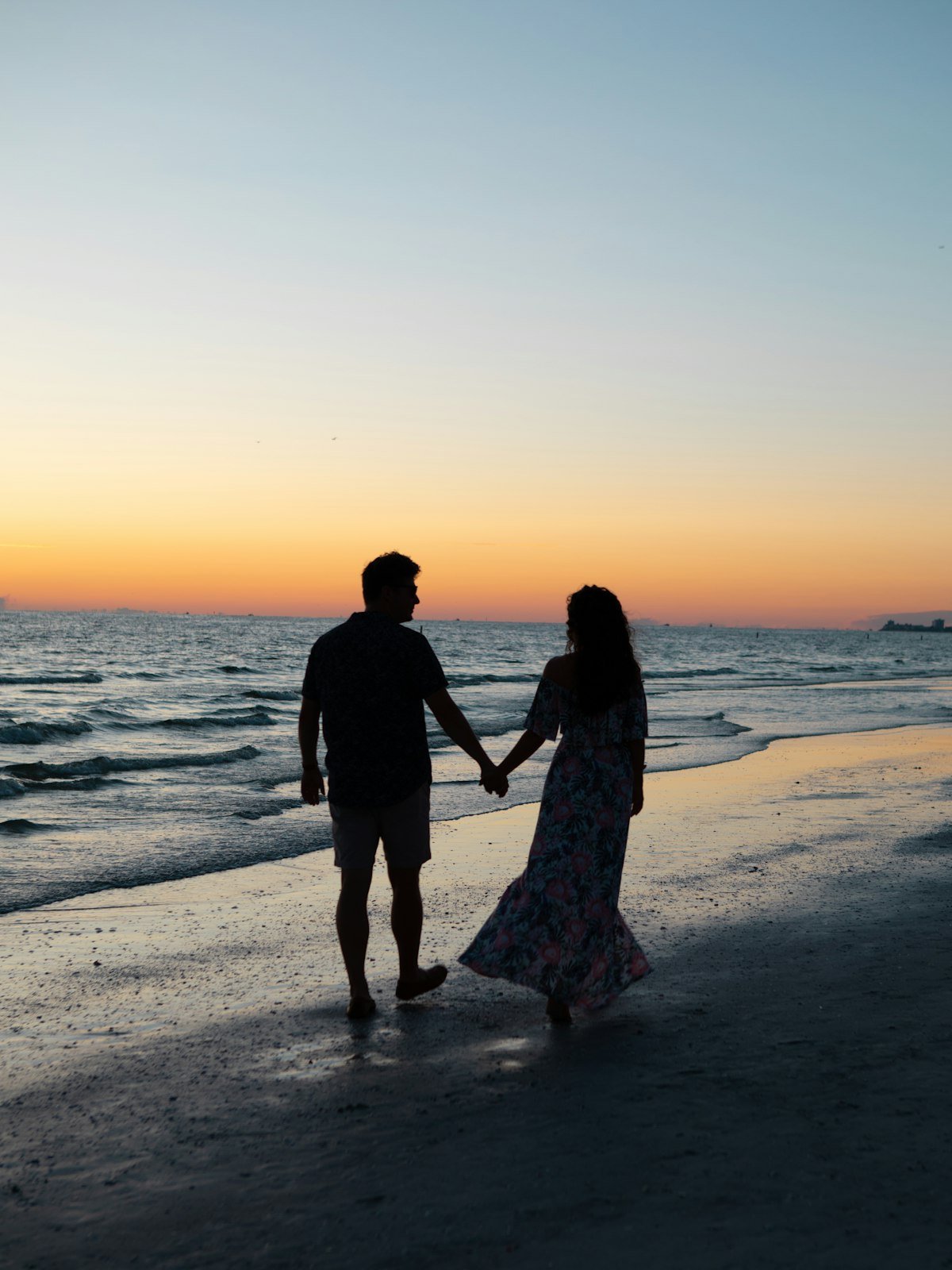 Couple walking hand in hand along the shore at sunset