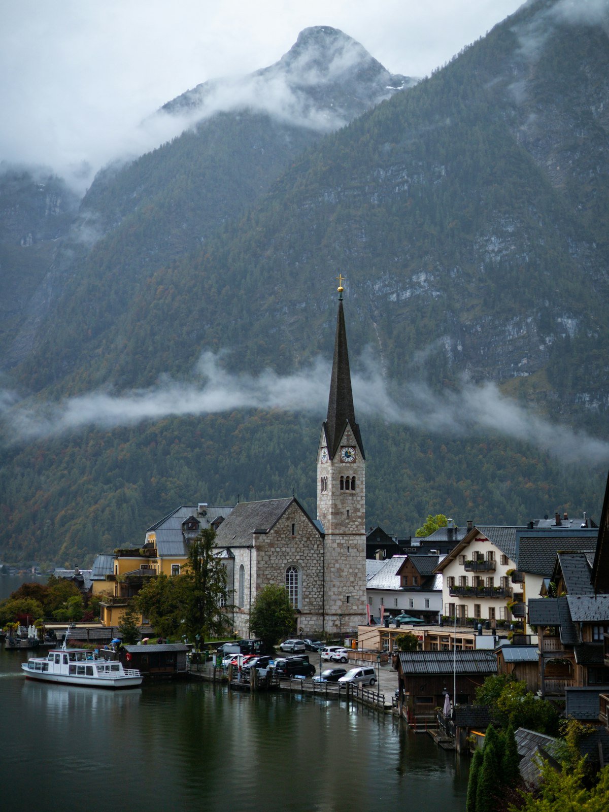 Lakeside alpine village with a church spire beneath misty mountains