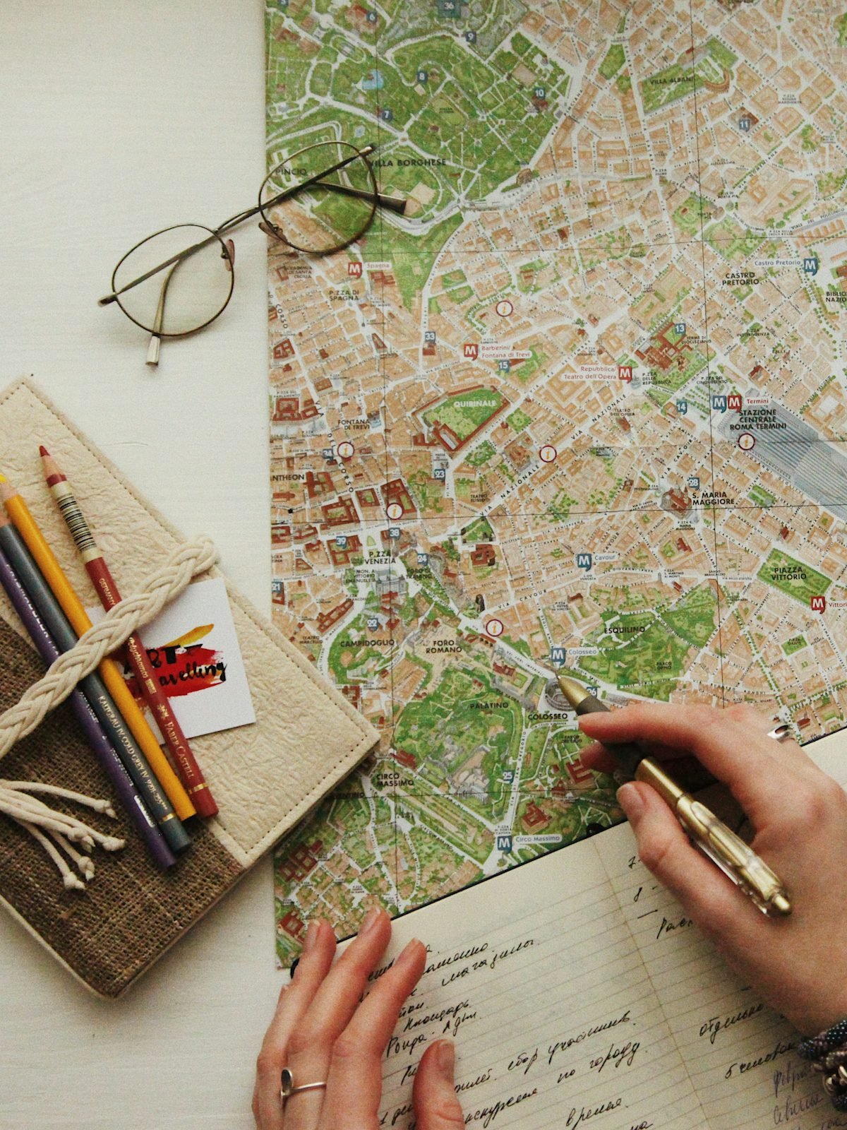Hands marking a route on a city map beside glasses and pencils